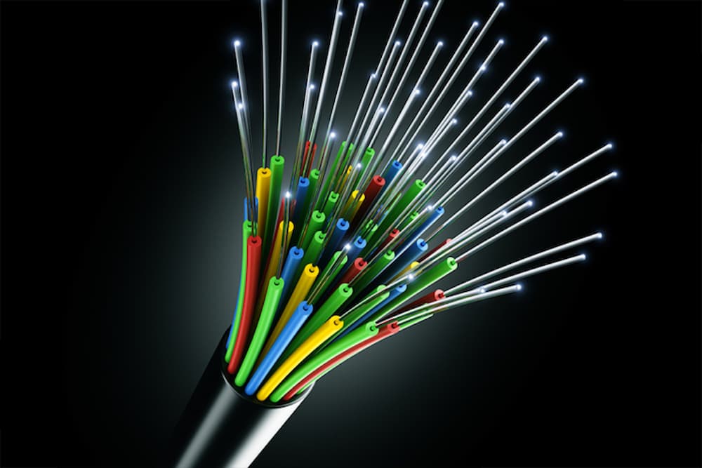 Close-up of fiber optic cables plugged into a network switch with vibrant teal connectors